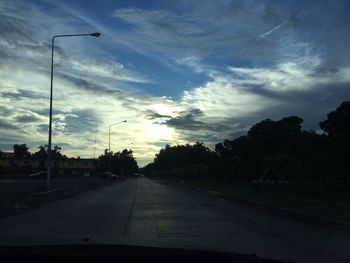 Road by trees against sky during sunset