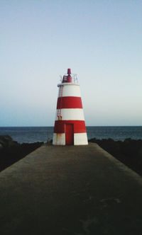 Lighthouse by sea against clear sky