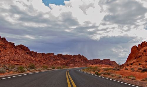 Empty road amidst rocky mountains against cloudy sky