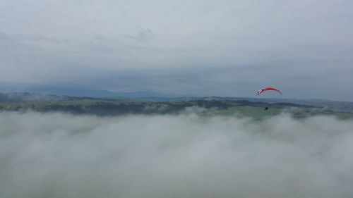 Person paragliding over mountain against sky