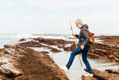 Full length of man on rock at beach against sky