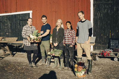 Portrait of multi-ethnic male and female farmers with organic vegetables standing outside barn