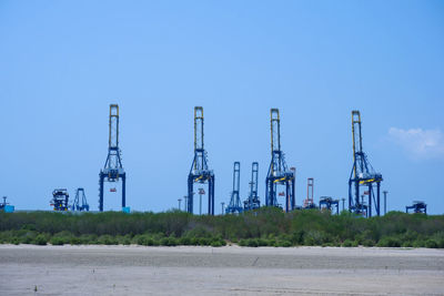 Electricity pylon by factory against clear blue sky