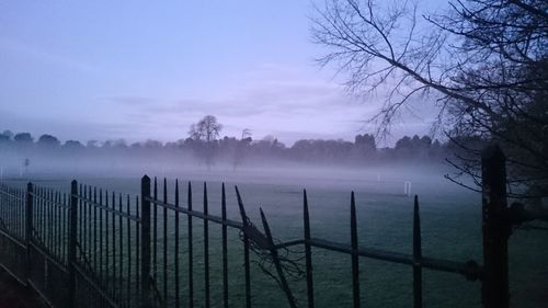 Wooden fence on field against sky during foggy weather