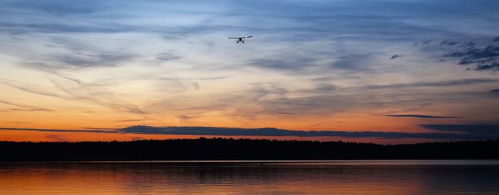 Silhouette of airplane flying over lake against sky