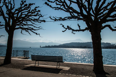 Empty bench by lake against sky