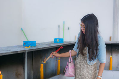 Young woman lighting incense sticks from candle