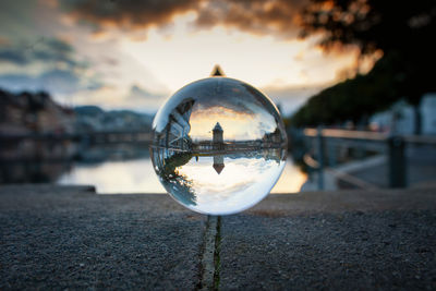 Close-up of crystal ball on water against cityscape during sunset