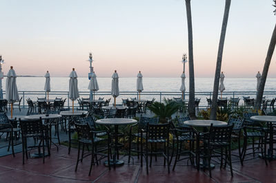 Tables and chairs at restaurant by sea at sunset