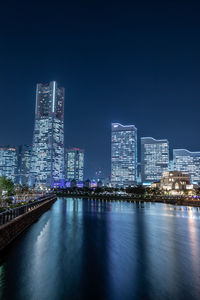 Illuminated buildings by river against sky in city at night