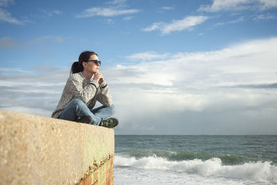 Side view of woman sitting on beach against sky