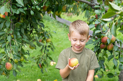 Boy holding apple against trees and plants