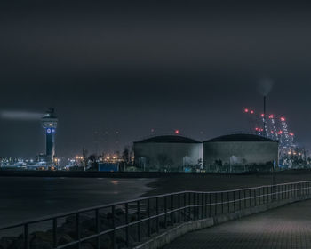 Illuminated bridge over river by buildings against sky at night