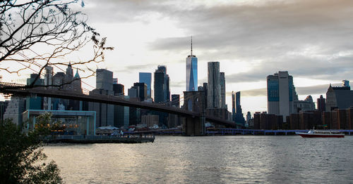 View of nyc skyline and brooklyn bridge river against cloudy sky