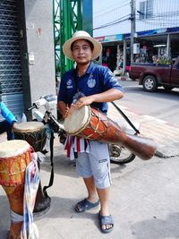 Portrait of man carrying drum while standing in city