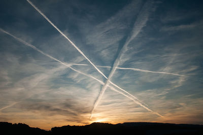 Low angle view of vapor trails in sky at sunset