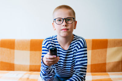 Teenage boy watching tv with glasses using tv remote while sitting on sofa