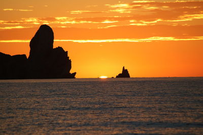 Silhouette rocks by sea against sky during sunset