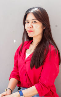 Portrait of young woman looking away while standing against wall