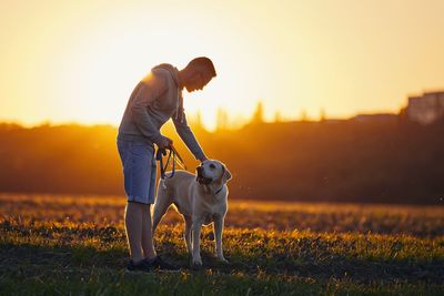 Man with dog on field against sky during sunset