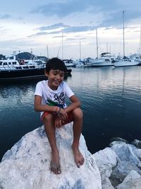 Portrait of boy sitting at harbor against sky
