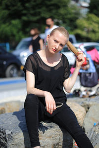 Portrait of young woman sitting on rock in city during sunny day