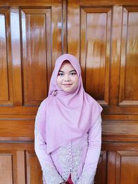 Portrait of smiling woman standing against pink wall