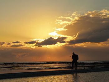 Silhouette man standing on beach against sky during sunset