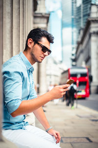 Side view of young man sitting in city