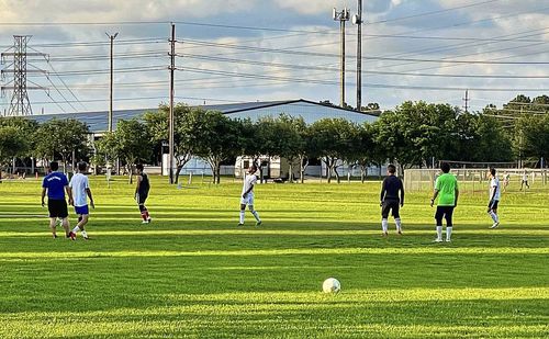 Group of people playing soccer on field against sky