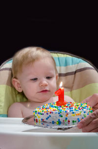 Baby girl looks at her first birthday cake, with a glowing candle on top