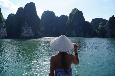 Rear view of woman looking at rock formation by sea against sky