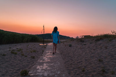 Rear view of man standing on land against sky during sunset