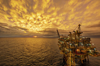 Offshore platform in sea against cloudy sky during sunset