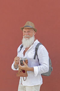 Portrait of man holding hat while standing against red wall