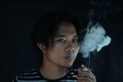 Close-up portrait of man smoking cigarette against black background