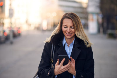 Smiling mature businesswoman using mobile phone while standing on street