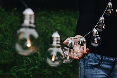 Midsection of man holding light bulb while standing on grassy field