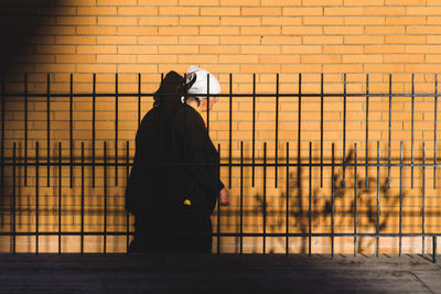 Man standing by railing against fence during sunset