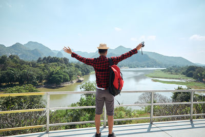 Rear view of man standing by railing on mountain against sky