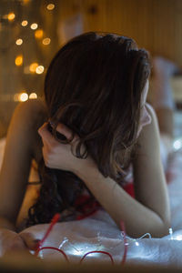 Young woman with illuminated string lights lying on bed at home