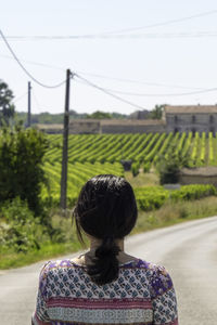 Rear view of woman standing on road against field during sunny day