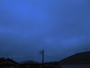 Low angle view of silhouette electricity pylon against blue sky