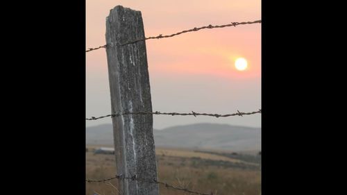 Barbed wire fence against sky during sunset