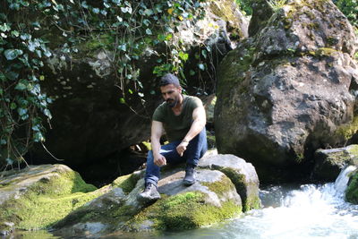 Full length of mid adult man sitting on rock by river