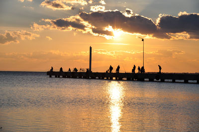 Silhouette people on sea against sky during sunset