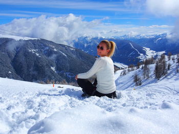 Portrait of young woman sitting on snow covered field against mountains