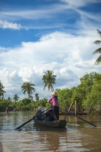 Man working on boat in river against sky