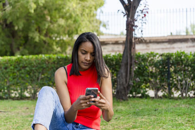 Young mother sitting on the grass, using mobile phone outdoors in a park.