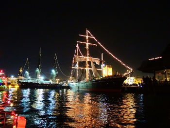 Illuminated suspension bridge over river against clear sky at night